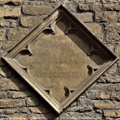 Close up of a diamond shaped stone plaque on a wall. Faint lettering says “Mechanics Institution mdcccxxxiii”